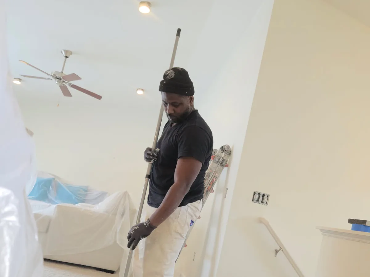 A painter rolling paint onto a ceiling in a bright room with drop cloths on the furniture