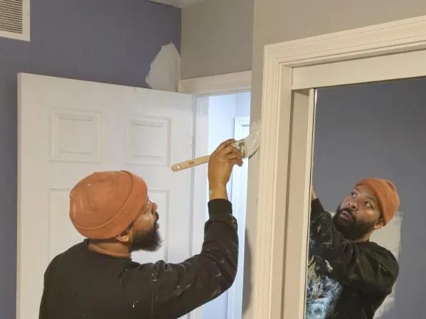 A painter brushing paint onto a door frame inside a home